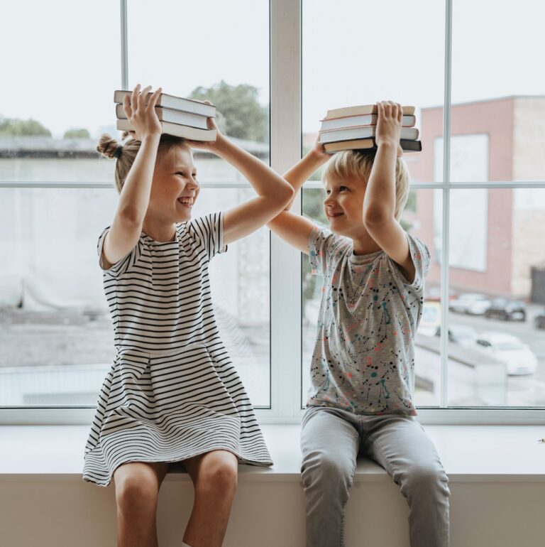 Dwoje dzieci patrzących się na siebie z książkami na głowach